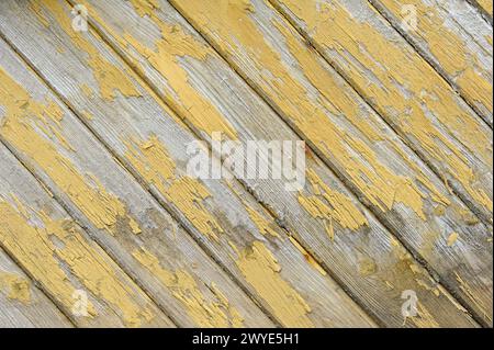 Diagonale Holzdielen zeigen verwitterte und abblätternde gelbe Farbe, die das Alter und die Witterungseinwirkung angibt. Stockfoto