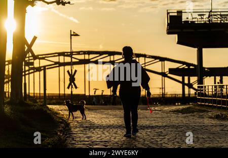 06. April 2024, Hessen, Frankfurt/Main: Eine Frau geht bei Sonnenaufgang im Osthafen mit ihrem Hund. Foto: Andreas Arnold/dpa Stockfoto