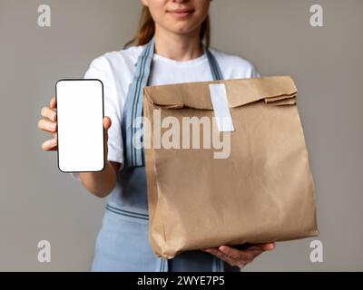 Mock-up-Banner für mobile App zur Bestellung und Lieferung von Lebensmitteln. Die Kellnerin hält ihr Handy mit leerem Bildschirm und Papiertüte zum Mitnehmen in der Hand. Stockfoto