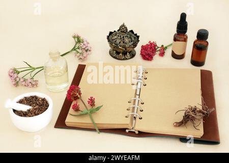 Baldrian-Kräuterwurzel mit Blumen, Notizbuch und ätherischen Ölflaschen. Wird in der pflanzlichen Medizin zur Behandlung von Schlaflosigkeit verwendet, ist ein Beruhigungsmittel und Beruhigungsmittel. Stockfoto