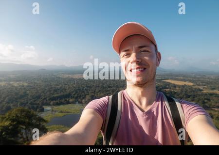 Glücklicher Mann, der Selfie vom Sommerferientag macht. Hübscher Tourist mit Mütze und einem Lächeln vor der Kamera vor tropischer Landschaft. Stockfoto