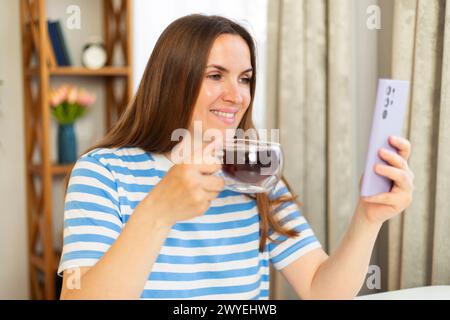 Frau, die eine transparente Tasse Tee hält, während sie ein Smartphone benutzt Stockfoto