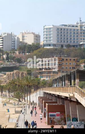 Tarragona, Spanien - 6. April 2024: Das Bild zeigt die Ruhe des Tarragona-Strandes mit verstreuten Besuchern, städtischer Architektur und Palmen, Reflle Stockfoto