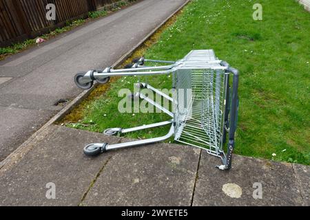 Ein verlassener Einkaufswagen an einem Grasrand in einer Stadt auf ihrer Seite neben Einem Pfad Stockfoto