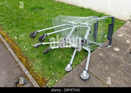 Ein verlassener Einkaufswagen an einem Grasrand in einer Stadt auf ihrer Seite neben Einem Pfad Stockfoto