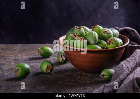 Tropische Früchte grüne reife Feijoa sellowiana Beeren in einer Tonschale und auf einem Tisch auf dunklem Hintergrund mit Kopierraum für Text Stockfoto