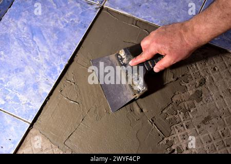 Nahaufnahme der Hände des Mannes, in einer sieht er einen Spachtel, mit dem er die Lösung auf den Boden aufträgt. Stockfoto