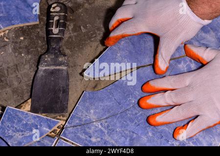 Ein Mann mit fusseligen Händen entfernt zerbrochene Keramikfliesen vom Boden. Stockfoto