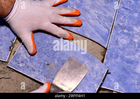 Der Meister mit einem Spachtel reißt die zerrissenen Keramikfliesen vom Boden im Bad ab. Stockfoto