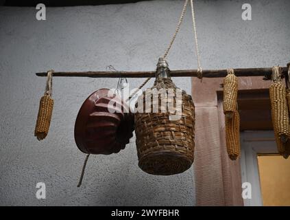 Antike Korbweinflasche, eine alte Gugelhupf-Backform und reife getrocknete Maiskolben an der Außenseite eines Landhauses in Riquewihr, Elsass Frankreich. Stockfoto