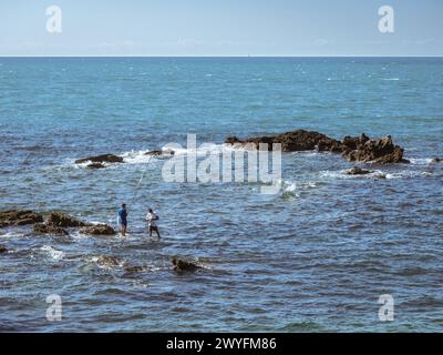 Cadiz, Spanien, 12. September 2023 - zwei Männer fischen mit Ruten im Meer, die auf Felsen gegen die Wellen stehen, Sommer, sonniges, ruhiges Wetter in Cadiz, Stockfoto