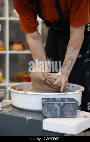 Nahaufnahme eines Mannes Hände, die eine Keramikvase auf einem Töpferrad brechen. Schule für Keramik. Vertikales Foto. Stockfoto