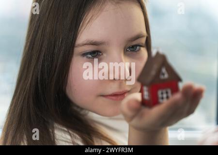 Kleines Teenager-Mädchen, das ein Modell eines Hauses ansieht. Er träumt von seinem eigenen Zuhause. Ausgewählter Fokus. Hochwertige Fotos Stockfoto