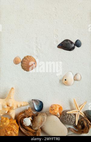 Fisch aus Muscheln und Kieselsteinen auf feinem Sand. Nachahmung der Unterwasserwelt. Draufsicht, flach. Stockfoto
