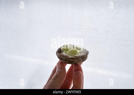 Detail einer Hand, die ein kleines Vogelnest mit drei kleinen grünen Ostereiern hält, gefüllt mit Schokolade. Es ist ein Osterbonbon-Tisch mit dem typischen Stockfoto