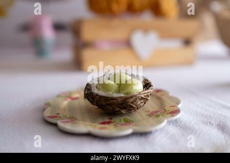 Detail eines Tellers mit einem kleinen Vogelnest mit drei kleinen grünen Ostereiern gefüllt mit Schokolade. Es ist ein Osterbonbon-Tisch mit dem typischen Stockfoto