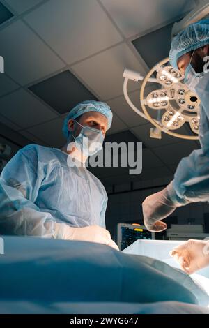 Tiefwinkelporträt eines chirurgischen Fachpatienten. Männliche Ärzte mit sterilen Handschuhen, chirurgischen Uniformen und chirurgischen Masken. Stockfoto