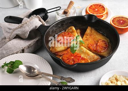 Crepes mit Orangensauce in einer gusseisernen Pfanne. Traditionelles französisches Crepe Suzette mit Orangensauce auf einem hellen Tisch Stockfoto