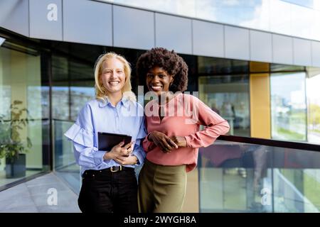 Zwei Frauen mit ähnlichen Merkmalen stehen nebeneinander, lächelnd, vor der großen Architektur. Stockfoto