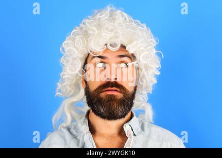 Porträt eines überraschten Mannes mit Bart und Schnurrbart in weißer Perücke. Partyzeit. Stilvolles bärtiges männliches Modell in lockiger Perücke. Modekonzept. Schöner Hipster Stockfoto