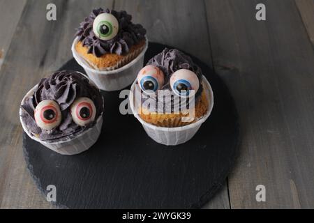 Drei Cupcakes mit grauer schwarzer Creme und Augen. Halloween-Feiertagsvorbereitung. Stockfoto