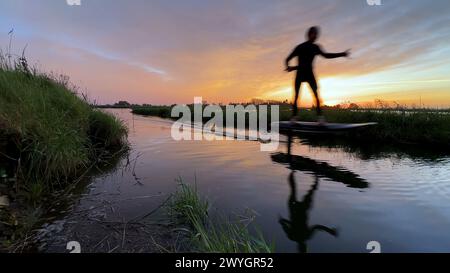 Tragflächenreiter gleitet mit seinem Brett in einem der Kanäle der Ria de Aveiro in Portugal während des Sonnenuntergangs über dem Wasser. Stockfoto