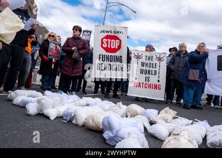 Demonstranten halten ein Banner mit der Aufschrift "die ganze Welt beobachtet" und "Juden sagen: Stoppen Sie die Finanzierung des Genozids" vor den auf dem Boden abgelegten Abbildungen. Eine kleine Gruppe von Demonstranten versammelte sich am Ende der Straße, in der Senator Chuck Schumer lebt, um ein sofortiges Ende aller US-Gelder für Israel zu fordern. Unter der Leitung der Aktivistengruppe Jewish Voice for Peace spaziert die Gruppe durch einen Bauernmarkt entlang des Prospect Park, auf dem Banner und Nachbildungen palästinensischer Kinder transportiert werden, die im Gaza-Streifen durch israelische Bombenangriffe im israelisch-Hamas-Krieg getötet wurden. Stockfoto