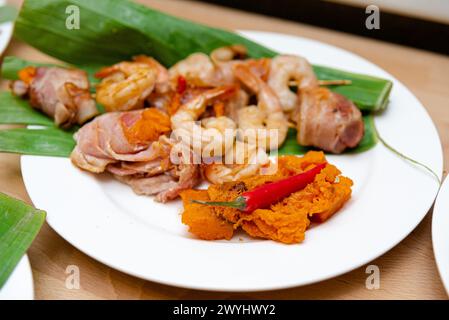 Saftige Garnelen und knuspriger Speck, serviert mit einer Beilage aus cremigem Kartoffelpüree, garniert mit Chili auf einem Bananenblatt. Stockfoto