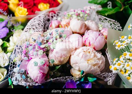 Exquisites Bouquet aus weichen rosafarbenen Pfingstrosen, ergänzt durch subtile Füllblumen und strukturierte Umhüllungen, die eine romantische Präsentation schaffen. Stockfoto