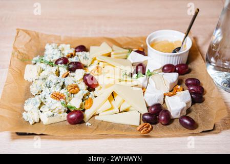 Eine gemischte Käseplatte mit Blauschimmelkäse, Brie, Cheddar, Trauben, Walnüssen, und Honig für ein Gourmet-Snack-Erlebnis. Stockfoto