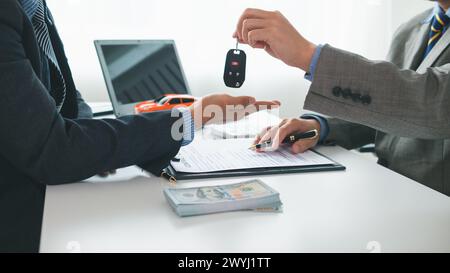 Der Autohändler übergibt dem Kunden Fahrzeugschlüssel, nachdem der Kaufvertrag und der Ratenzahlungsvertrag unterzeichnet wurden. Konzept der Übergabe von Autoschlüsseln an cu Stockfoto