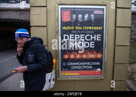 Moskau, Russland. 6. April, 2024. Ein Mann raucht auf einem Hintergrund eines Werbebanner des Rockkonzerts des Depeche Mode englische elektronische Musik auf einer Straße im Zentrum von Moskau, Russland Stockfoto