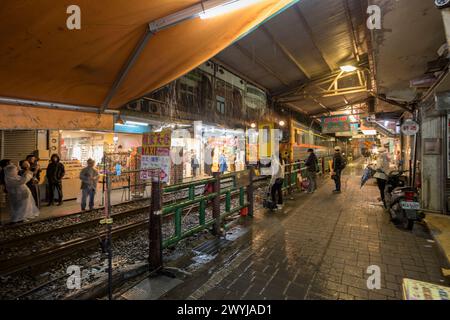 Nachtzug, der durch die engen Gassen von Shifen fährt, während Passanten Fotos machen und warten, um die Gleise zu überqueren Stockfoto