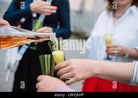 Eine Frau gießt Wein in zwei grüne Gläser. Die Gläser sind mit Wein gefüllt und die Frau hält sie an den Mund. Die Szene spielt in A Stockfoto