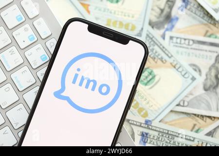KIEW, UKRAINE - 1. APRIL 2024 IMO-Messenger-Symbol auf dem Smartphone-Bildschirm auf vielen usd-Geldrechnungen. IPhone-Display mit App-Logo und Dollarscheine mit weißer Tastatur Stockfoto
