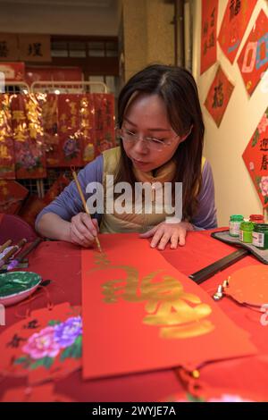 Eine fokussierte Frau schreibt traditionelle chinesische Kalligraphie auf rotes Papier und wünscht sich das neue Jahr Stockfoto