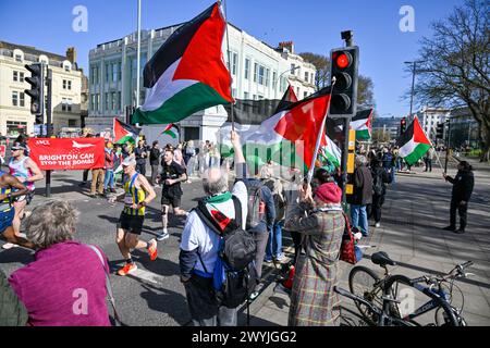 Brighton UK 7. April 2024 - Pro Palestine Protestierende schwenken Flaggen, während Tausende von Läufern an einem hellen und sonnigen, aber windigen Tag am Brighton Marathon teilnehmen : Credit Simon Dack / Alamy Live News Stockfoto