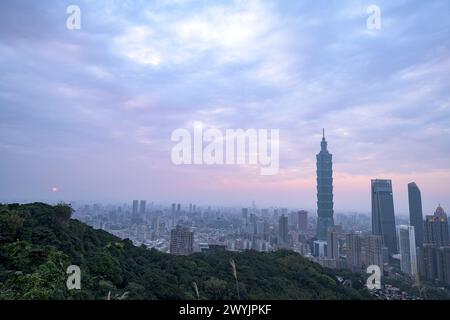 Ein erhöhter Blick auf Taipeh Stadt während der Dämmerung mit Wolkenkratzern vor einem subtilen Sonnenuntergang, aufgenommen von einem bergigen Gebiet mit Laub Stockfoto