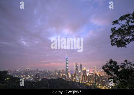 Ein erhöhter Blick auf Taipeh Stadt während der Dämmerung mit Wolkenkratzern vor einem subtilen Sonnenuntergang, aufgenommen von einem bergigen Gebiet mit Laub Stockfoto