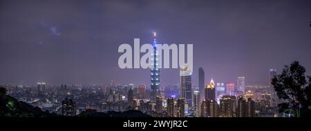 Ein erhöhter Blick auf Taipeh Stadt während der Dämmerung mit Wolkenkratzern vor einem subtilen Sonnenuntergang, aufgenommen von einem bergigen Gebiet mit Laub Stockfoto