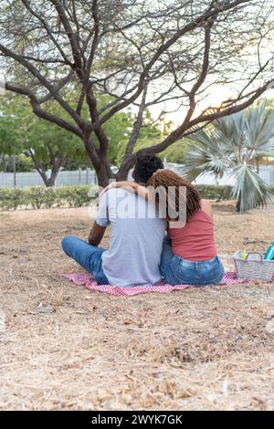 Rückansicht eines Paares in einer Umarmung, bei einem Picknick in der Abenddämmerung. Stockfoto
