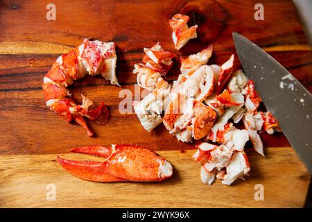 Gekochtes Fleisch mit rotem Hummer auf einem hölzernen Schneidebrett. Messer und schneiden Sie Schwanz und Klauen auf Holzoberfläche in Stücke Stockfoto