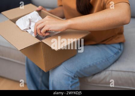 Happy Girl erkundet das gelieferte Paket, bestätigt die Zufriedenheit des Online-Einkaufs und der Lieferung nach Hause. Stockfoto