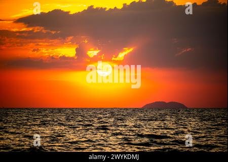 Feuriger Horizont, dramatischer Sonnenuntergang im Ozean in lebendigen Farben über dunklem Wasser, atemberaubendes Naturfoto, das die Kunstfertigkeit des ruhigen Spektakels der Abenddämmerung reflektiert und Stockfoto