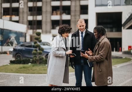 Drei junge, vielfältige Geschäftsleute führen ein gemeinsames Gespräch außerhalb eines modernen Bürogebäudes. Stockfoto