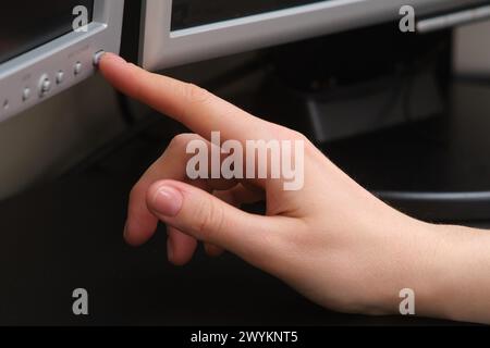 Die Hand einer Frau drückt den ein-/Ausschalter auf einem Computermonitor Stockfoto