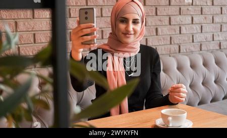 Selfie im Café. Online-Stream. Hübsche Frau im Hijab macht Fotos und erstellt Inhalte für Blog-Internetgespräche in einem gemütlichen Café. Stockfoto