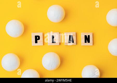 Ein gelber Hintergrund mit einer großen Gruppe weißer Kugeln, die um ihn herum verstreut sind. Das Wort Plan ist in schwarzen Buchstaben auf die Kugeln geschrieben, wodurch ein p entsteht Stockfoto