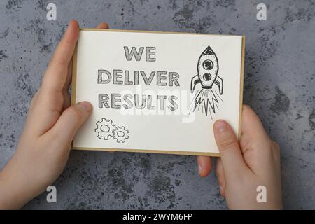 Eine Hand, die ein Blatt Papier hält, auf dem die Worte „Wir liefern Ergebnisse“ geschrieben sind. Auf dem Papier befindet sich auch eine Rakete Stockfoto