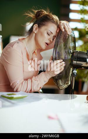 Nachhaltiger Arbeitsplatz. Moderne Geschäftsfrau mittleren Alters bei der Arbeit mit elektrischem Ventilator, der unter Sommerhitze leidet. Stockfoto